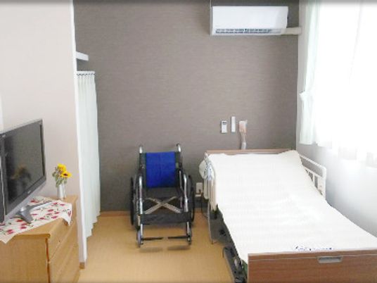 寝具付きのベッドやタンス、テレビなどが置かれた部屋には車いすもあり、エアコンも付いている。