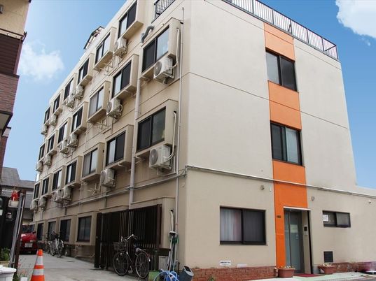 施設外観は全体的にベージュだが、側面に１本オレンジの縦ラインが入っている。４階建ての頑丈な建物。