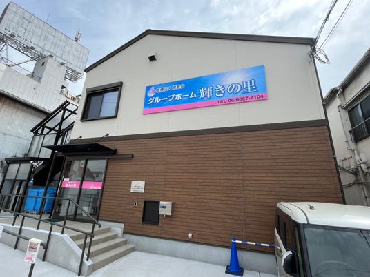 フロアで外壁の色が異なる２階建ての建物。玄関には手すり付きのスロープと階段が設置されている。