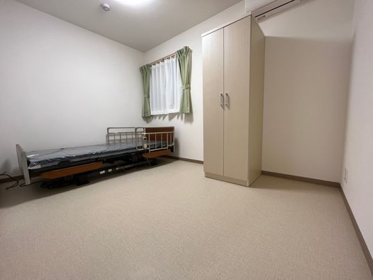 クローゼットが置かれた部屋には介護ベッドやレースカーテンとカーテンが付いた窓がある。
