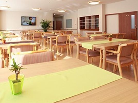 四人掛けのテーブルと椅子が並べられている施設内のリビングスペースの様子