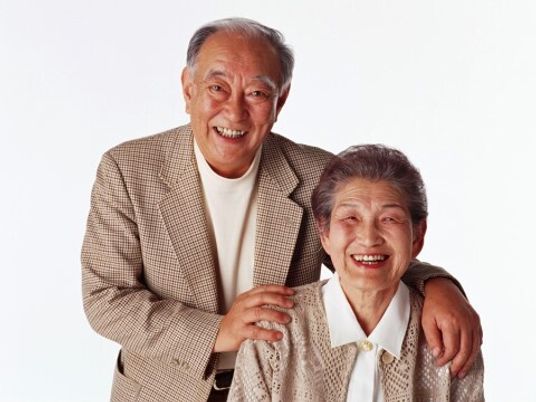 高齢者夫妻がこちらを向いて微笑んでいる様子。男性が女性の方に手をまわしている