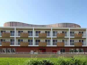 周辺を田畑に囲まれたのどかな環境。３階建ての建物は横に長く、屋上に柵がある。