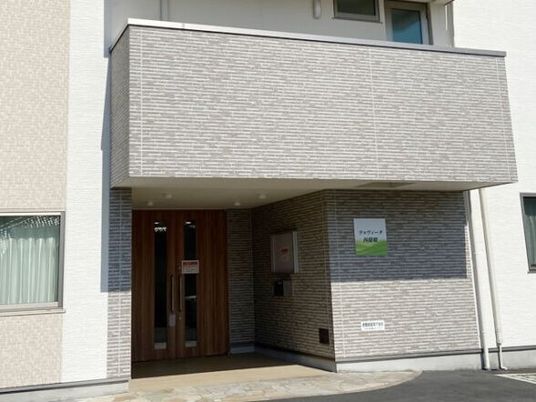 グレーの外壁の重厚感のある建物の玄関には住宅名が書かれたプレートが貼られ、段差もない。