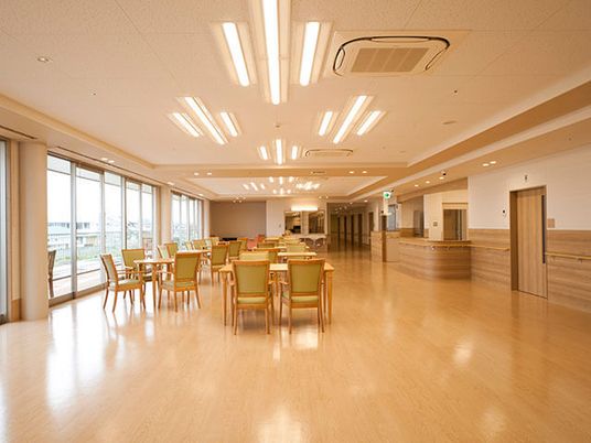 広々とした明るい食堂。木製のダイニングテーブルセットが並んでいて、奥にはキッチンもある。