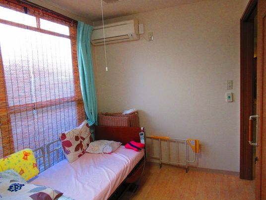 寝具がセットされたベッドが置かれた畳敷きの部屋にはエアコンもある。大きな窓にはすだれも付いている。