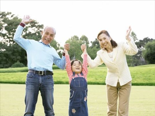 晴れた天気のもと、孫と祖父祖母が手を取り合って手を挙げている様子。