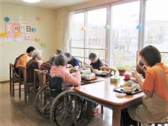 オレンジのポロシャツを着たスタッフが入居者と食卓を囲んでいる。