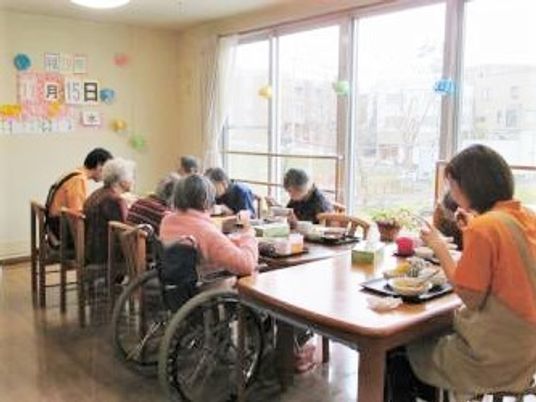 オレンジのポロシャツを着たスタッフが入居者と食卓を囲んでいる。