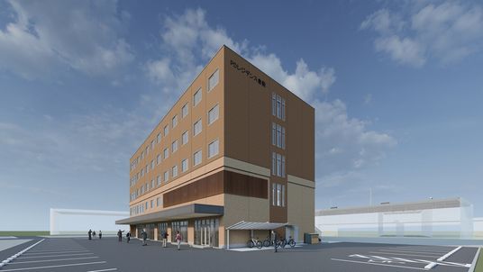 広い駐車スペースがあり、茶色い外壁の5階建て建築物