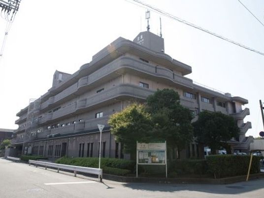 道路の面した4階建てのブラウン系の建物周りには緑も多く植えられ、案内看板も設置されている。