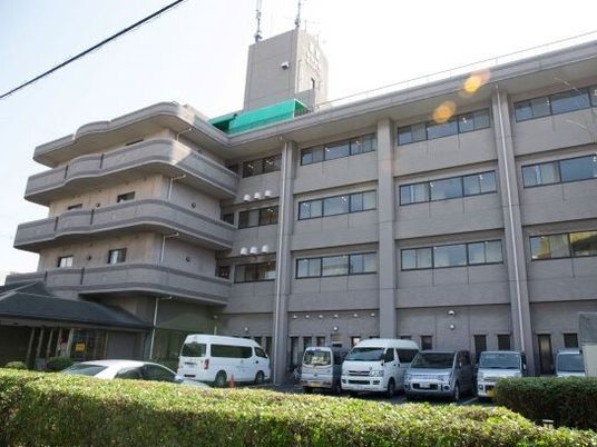 ブラウン系の建物の周りには緑が植えられ駐車場もあり、一部屋上には緑の屋根のようなものが設置されている。