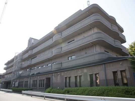 各フロアにベランダが設置された4階建ての建物。落ち着いたブラウン系でまとめられ、緑も植えられている。