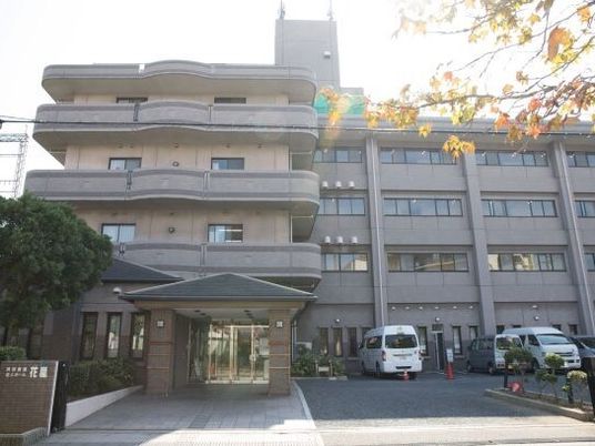 4階建ての建物はブラウン系で広い駐車場やベランダもあり、玄関には三角屋根がついている。