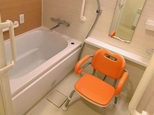 一人用の浴槽とオレンジ色のシャワーチェア、そしてシャワーがそろった浴室。