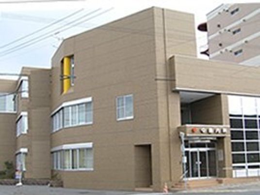 白とブラウンを基調とした2階建ての建物。2階部分にはテラスがあり、玄関には屋根が付き、庭も用意されている。建物の上には青空が広がっている。