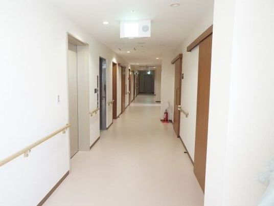 両サイドに手すりが設置された白い廊下。エレベーターや消火器もある。