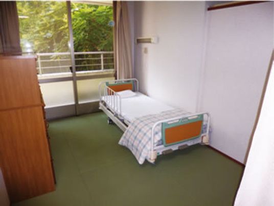 寝具付きのベッドやタンスが置かれている部屋にはカーテンが付いた大きな窓があり、緑あふれる風景が見える。