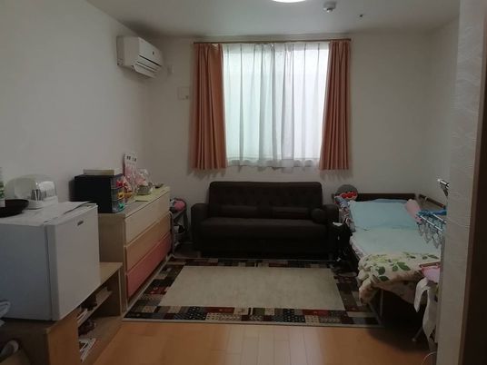 エアコンが付いたフローリングの部屋には寝具付きのベッドやタンス、ソファなどがあり、小さな冷蔵庫も置かれている。