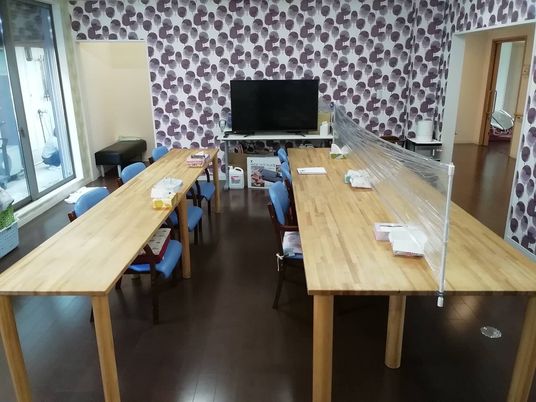 木製のダイニングテーブルが二組置かれた食堂にはテレビもあり、テーブルの一つにはアクリル板が設置されている。