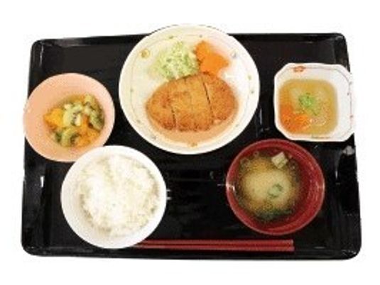 おいしそうな食事が並んだトレー。とんかつに白いご飯、みそ汁、そしてフルーツや野菜。