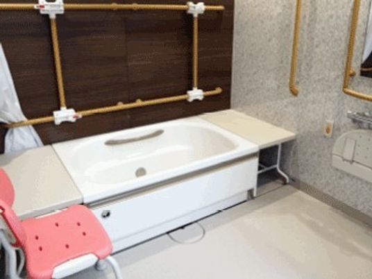 白い浴槽やシャワーが設置された浴室。シャワーチェアや手すりも設置されている。