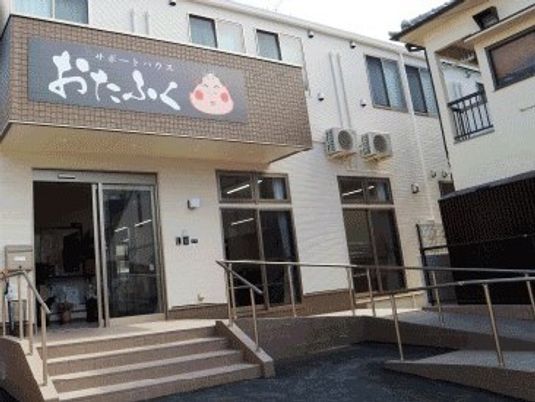 おたふくのイラストが描かれた屋根が付いた建物は2階建て。玄関先にはスロープや階段がある。