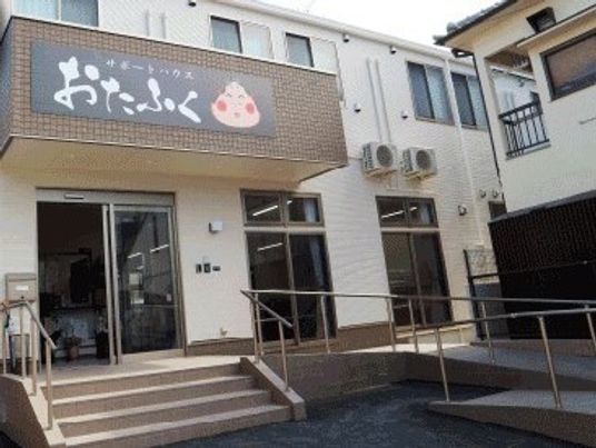 おたふくのイラストが描かれた屋根が付いた建物は2階建て。玄関先にはスロープや階段がある。