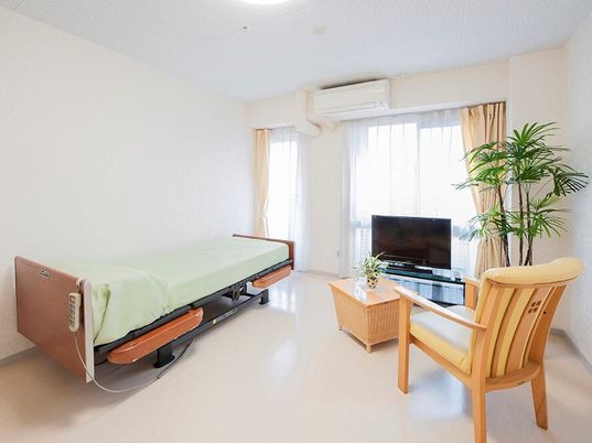 介護ベッドやエアコン、テレビ、一人用のいすが置かれた部屋にはカーテン付きの窓もある。