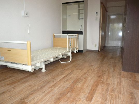 ベッドサイドには緊急通報装置が付いたフローリングの部屋には介護ベッドやキッチンがある。