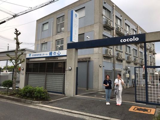 3階建ての建物はグレーを基調としたどっしりとした造り。建物の前には女性が二名立っている。