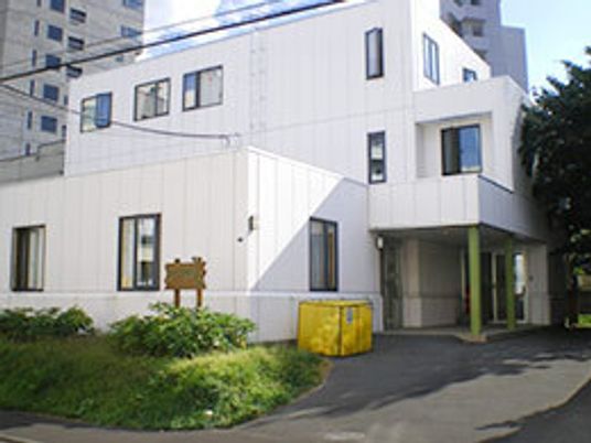 角ばった白を基調とした3階建ての建物は周りに適度に緑が植えられ、後ろの方には背の高いビルが建ち並んでいる。玄関には屋根が付いている。