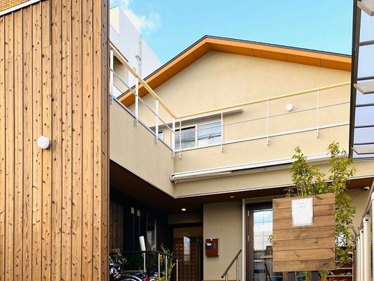 三角屋根がついた２階建ての建物は、ベージュ系で家庭的な雰囲気。広いテラスも付いている。
