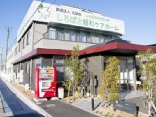 自動販売機が設置されている敷地内には沢山の木が植えられている。2階建ての建物はグレー系の外観。
