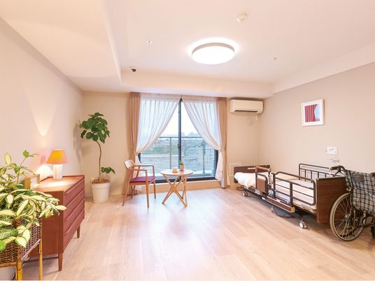 寝具付きのベッドやタンス、テーブルセットなどが置かれているフローリングの部屋。大きな窓も付いている。