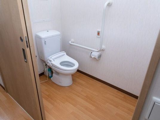 エル字型の手すりがついた介護仕様のトイレの様子。緊急コールがついた壁がある