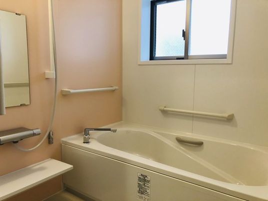 一人用の浴槽が置かれた浴室。手すりや窓、シャワーも設置されている。
