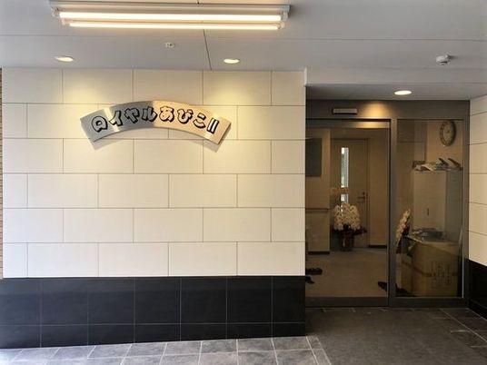 白い外壁にはホーム名が書かれたプレートが貼られ、エントランスには自動ドアが設置されている。