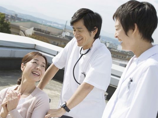 車いすの女性とそれを押している医師と看護師。天気の良い日の写真