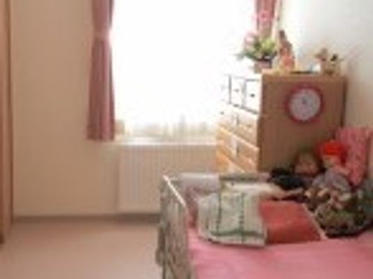 ベッドやたんす、パネルヒーターが置かれた居室。カーテンが付いた大きな窓がある。