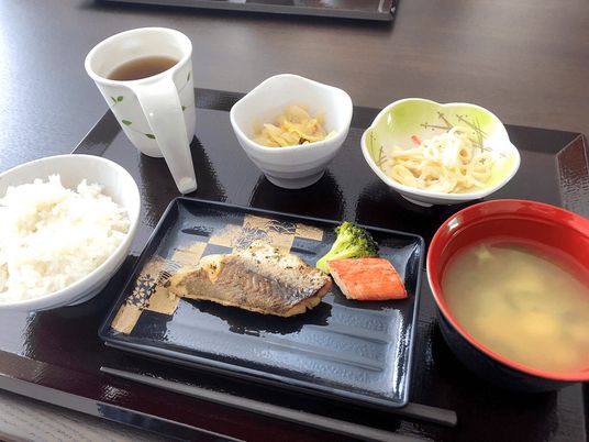 魚料理がメインの食事例。白いご飯や野菜の煮物、みそ汁やお茶などが並んでいる。