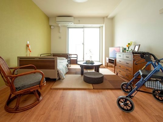 歩行器やベッド、エアコンやタンスなどの家具が付いた部屋は明るく、フローリングで段差がない。
