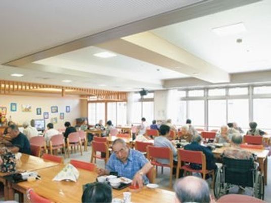 広いホールのような空間に高齢者が集まってくつろいでいる様子。施設内の一場面