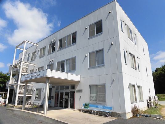 鉄骨造３階建ての建物の様子。ホワイトを基調にした外観、エントランス部分に雨除けのひさし