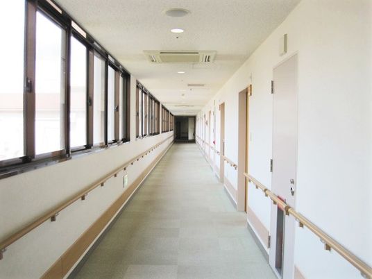 廊下には手すりが設置され、右側には居室、左側には窓があり、明るい雰囲気。