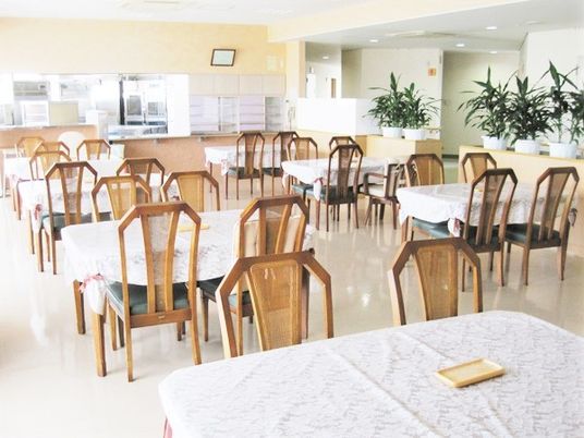 テーブルクロスがセットされた4人掛けのテーブルが複数並ぶ食堂からは厨房も見える。