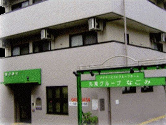 グレー系の外観の3階建ての建物の各フロアにベランダがあり、ホーム名が書かれたアーチなどがある。