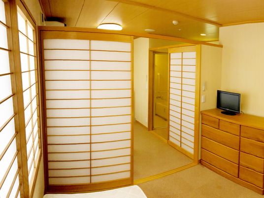 障子が設置された居室内にはタンスがあり、その上にはテレビが置かれ、奥には浴室もある。