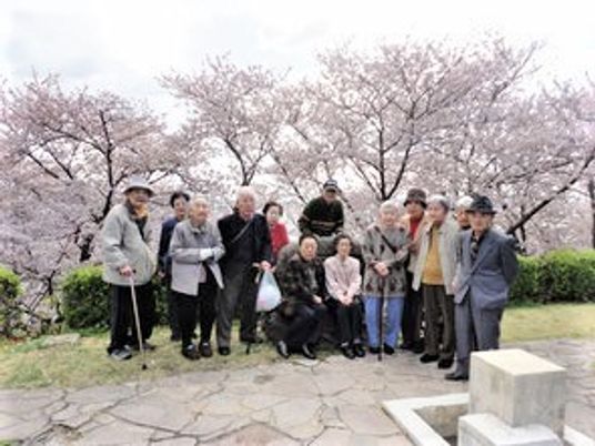 桜の花の下で微笑む老人ホームの入居者。春の行事の際の１枚