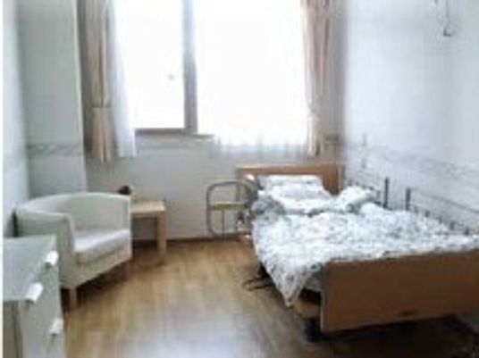 寝具付きのベッドやいすが置かれたフローリングの居室には大きな窓が付き明るい雰囲気。